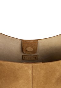 Intérieur de sac en daim beige avec une texture lisse, doté d'une fermeture magnétique et d'une étiquette indiquant "nat & nin". Design épuré et minimaliste.