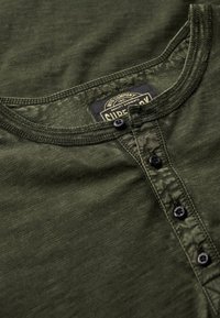 Groene henley shirt met een ronde halslijn, een vijfknopen sluiting en een textuurstof. Etikettag zichtbaar nabij de kraag.