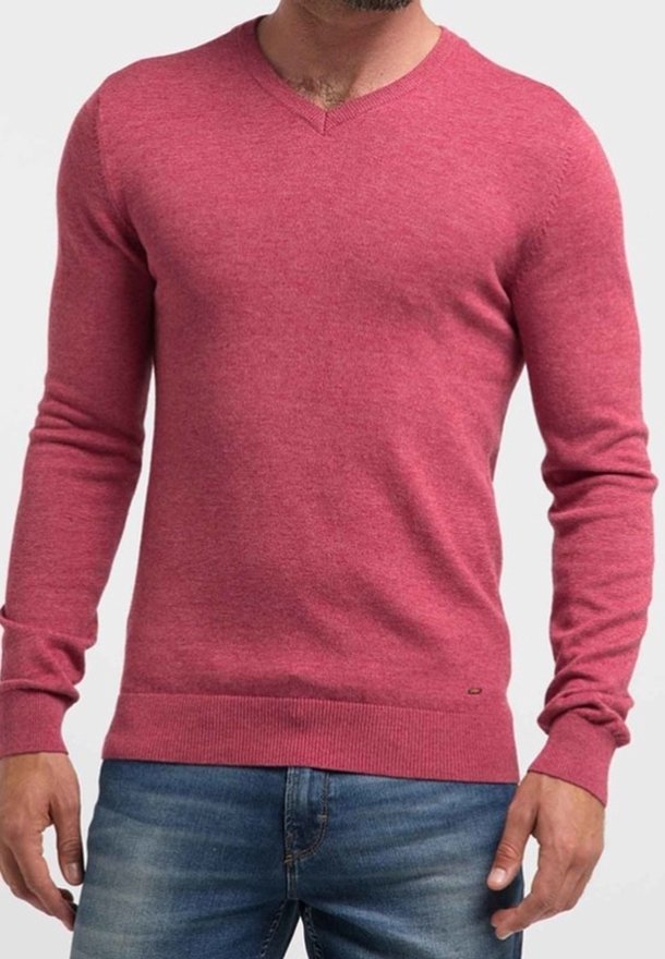 Pull rouge à col en V en tissu doux, avec manches longues et ourlet côtelé. Porté avec un jean bleu, montrant une silhouette ajustée.