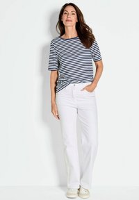 Navy en witte gestreepte t-shirt met korte mouwen, gecombineerd met witte broek. De outfit omvat casual witte sneakers en heeft een ontspannen pasvorm.