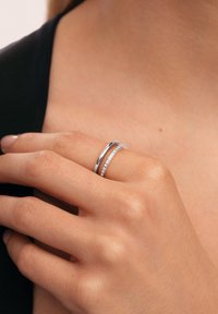 Set di anelli in argento composto da una fascia liscia e una fascia pavé con piccole pietre trasparenti, indossati su una mano con finitura naturale delle unghie.