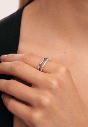 Set di anelli in argento composto da una fascia liscia e una fascia pavé con piccole pietre trasparenti, indossati su una mano con finitura naturale delle unghie.