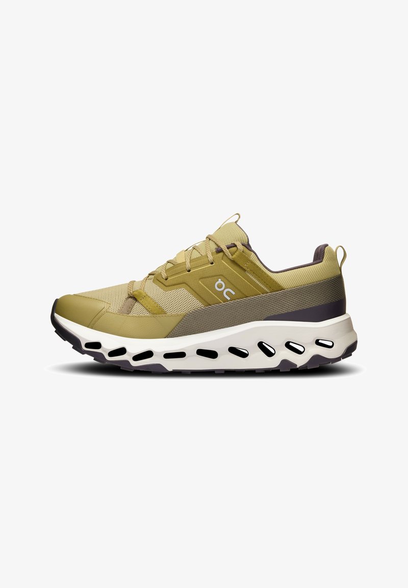 Chaussure de sport légère vert olive clair et beige avec semelle blanche, détails noirs ovales découpés, empeigne en mesh et logo latéral.