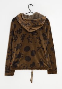 Veste à capuche marron avec un intérieur doux et texturé, ornée de motifs graphiques noirs de étoiles, formes et figures sur une surface lisse.