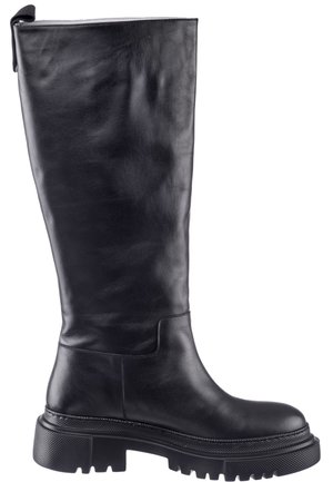 Femme portant un gilet en cuir noir sans manches surdimensionné avec ceinture, un haut noir à manches longues, un pantalon en cuir et des bottes noires montant jusqu'aux genoux sur fond blanc.
