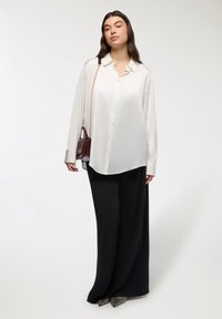 Camicia bianca leggera con maniche lunghe, abbinata a pantaloni neri a gamba larga e una piccola borsa a tracolla color bordeaux. Tacchi testurizzati.