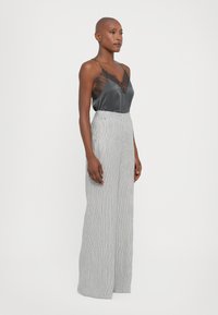 Gray satin camisole with black lace trim, paired with high-waisted, wide-leg striped pants; smooth texture, minimalistic design.