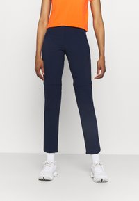 Marineblauwe sportbroek met een taps toelopende pasvorm en ritsen op de knieën, gemaakt van rekbaar materiaal. Gecombineerd met een feloranje crop-top en witte sneakers.