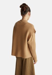 Volný, ribbovaný svetr v teplé béžové barvě, se štíhlým krkem a širokými rukávy. Měkká textura s pohodlným, nadměrným střihem.