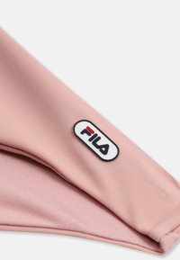 Gros plan sur un tissu rose avec un patch du logo de la marque Fila cousu sur un bord plié.