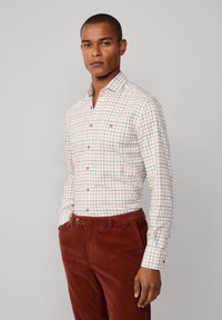 Witte knop-up shirt met een rood en groen ruitpatroon, gecombineerd met bruine corduroy broek. Voorzien van een kraag en knoopdetails aan de voorkant.