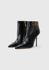Black leather ankle boots with pointed toes, high stiletto heels, gold hardware detail on the side, and a smooth texture.