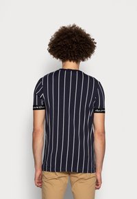 Marinblå, kortärmad t-shirt med vertikala vita randiga mönster och svarta detaljer på ärmarna med text. Mjuk bomullsmaterial.