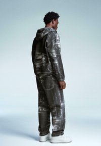 Gray denim tracksuit with a hooded jacket and elastic cuffs, featuring a textured, faded pattern. Paired with white athletic shoes.