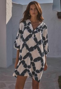 Bijela tunika s mornarskim tie-dye uzorkom, s v-izrezom i rukavima do tri četvrtine, napravljena od lagane tkanine s opuštenim krojem.
