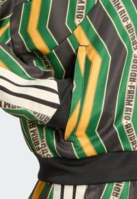 Veste à motifs verts, noirs et jaunes avec des designs en chevron, poignets élastiques et une poche rentrante avec des accents côtelés noirs.