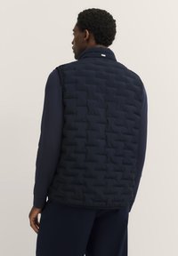 Marineblau gepolsterte Weste mit hohem Kragen und gestepptem Design, ohne Ärmel und mit einem dezenten Markenschild am Kragen.