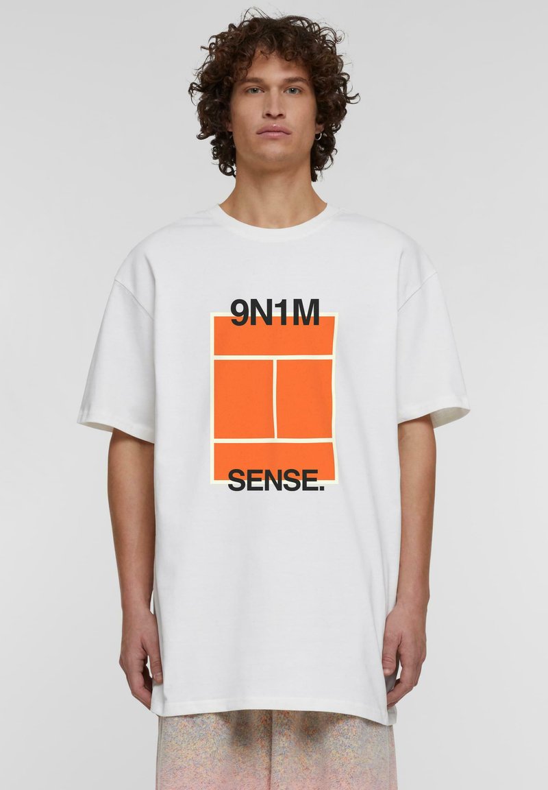Balts pārspīlēts t-krekls ar grafisku dizainu, kurā ir oranži un melni elementi, teksts "9N1M SENSE" spēcīgās burtu formās.