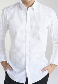 Biała koszula w małe czarne kropki, zapinana na guziki, z długimi rękawami z mankietami oraz gładką teksturą. Prosty kołnierzyk i prosta dolna krawędź.