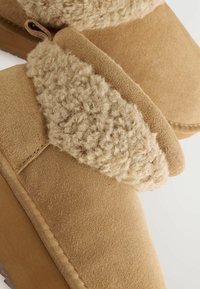 Tan ruskind ankle støvler med en fluffy beige shearling manchet. Glat tekstur med en fleksibel gummIsål og diskret syning.