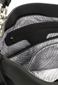 Schwarzes Tascheninnere mit glatter Textur, ausgestattet mit einem Reißverschlussfach und einem bedruckten Futter mit grauem Text, einschließlich des Markennamens SURI FREY.