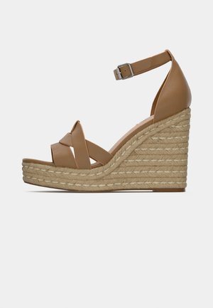 Tan leather wedge sandal featuring a braided jute platform, cross straps, and an adjustable ankle strap.