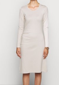 Dlouhý rukáv, šaty po kolena ze světle béžové tkaniny. Mají kulatý výstřih a přímou siluetu, s minimální texturou a bez vzorů.