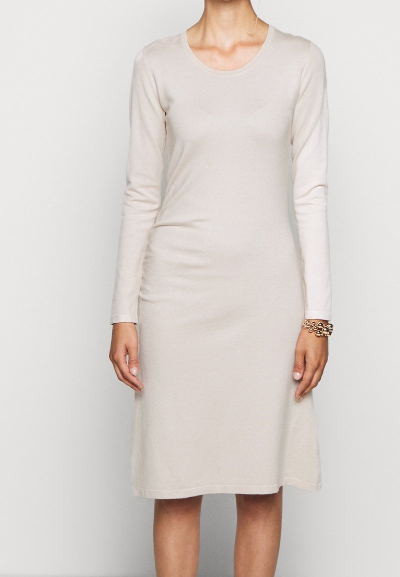 Dlouhý rukáv, šaty po kolena ze světle béžové tkaniny. Mají kulatý výstřih a přímou siluetu, s minimální texturou a bez vzorů.