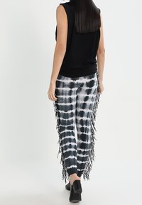 Haut sans manches noir associé à un pantalon tie-dye avec des motifs noir et blanc, des détails à franges sur les côtés et une coupe ajustée.