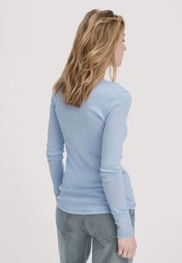 Lichtblauw overhemd met lange mouwen, een aansluitend ontwerp, een gladde textuur en een ronde halslijn, gecombineerd met hoge taille blauwe jeans.