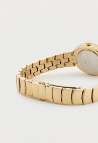 Ρολόι Calvin Klein από μεταλλικό υλικό με χρυσή απόχρωση, με βραχιόλι με συνδέσμους και κούμπωμα, εμφανίζεται σε ανοιχτό φόντο, οπίσθια όψη ορατή.