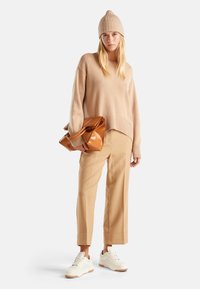 Beige gebreide trui met ribbelzoom, crèmekleurige broek met wijde pijpen en glanzige bruine handtas, aangevuld met witte sneakers.