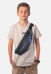 Borsa a tracolla nera e blu con un design testurizzato, dotata di un logo prominente e una tracolla regolabile, indossata da una persona con una camicia chiara.