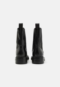 Black leather ankle boots with elastic side panels, flat black soles, and pull tabs at the back. Smooth texture and rounded toe design.