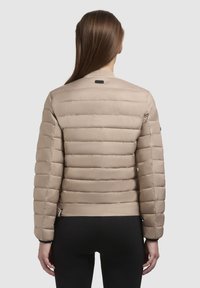 Giacca piumino beige con design trapuntato, colletto a coste e polsini elastici. Realizzata in un materiale liscio e leggero, dotata di un design con cintura.