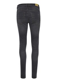 Jean skinny en denim foncé avec une texture lisse, présentant des coutures détaillées sur les poches arrière et une coupe ajustée sur les jambes.