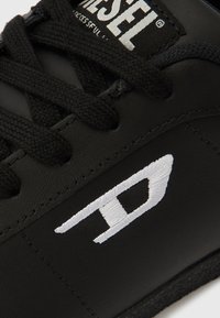 Čierny kožený tenisky s čiernymi šnúrkami, zdobené bielym vyšívaným logom a prešívaním. Hladká textúra s nízkym profilom.