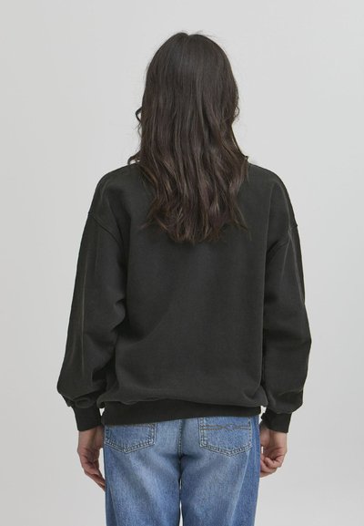 Svarte sweatshirt med droppede skuldre og ribbede kanter, kombinert med lyseblå denim jeans. Tøyet ser mykt og litt strukturert ut.