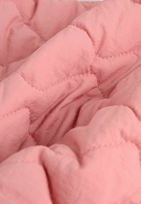 Coperta trapuntata rosa chiaro con una consistenza morbida e liscia, caratterizzata da motivi cuciti e un aspetto morbido e soffice.