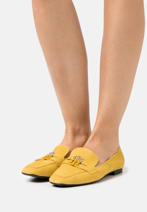 Ballerine gialle in camoscio con punta affusolata, dettagli decorativi con fibbia e suola nera a profilo basso, mostrante una texture liscia.