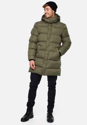 Olive green puffer coat with a hood, quilted texture, zip closure, and side pockets, paired with black pants and boots.