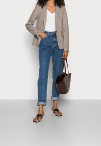 Blazer textured color marrone chiaro sopra una maglietta bianca a V, abbinato a jeans in denim blu arrotolati e una borsa a tracolla intrecciata marrone scuro. Sandali neri.