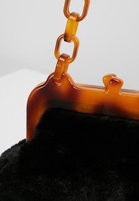 Hnědá a černá kabelka s huňatou texturou, odvážným řetězovým popruhem a zdobeným rámem. Vyrobena z udržitelných materiálů.