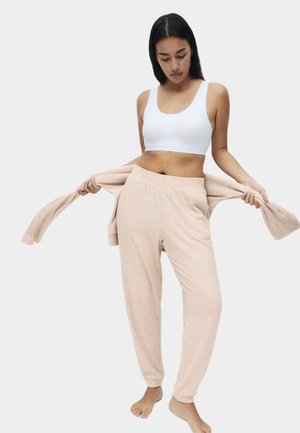 Lyserød ribbet loungewear-sæt med en cropped tanktop og højhalsede bukser med manchetter, lavet af blødt, tekstureret stof.