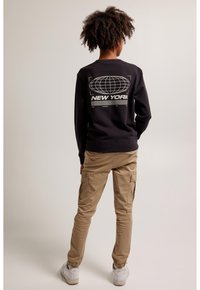 Mustat collegepaidat, joissa on globaali grafiikka ja "NEW YORK" takana, yhdistettynä khaki-värisiin cargo-housuihin ja valkoisiin tennareihin.