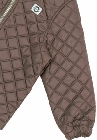 Manche d'une veste matelassée marron avec poignets élastiques et fermeture éclair argentée, avec un petit patch logo blanc près de l'épaule.