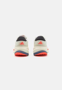 Sneaker Adidas di colore grigio chiaro con accenti rossi. Presentano una tomaia in mesh texturizzato, colletto imbottito e una suola a contrasto blu e rossa.