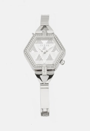 Ezüst hatszögletű óra mintás számlappal, kristályos díszítéssel és fém szíjjal. Minimalista dizájn, kapcsos záródással.