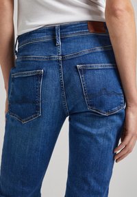 Blå denimjeans med midjehöjd, rundad söm på bakfickorna och en läderlogotyp på bakre midjan.