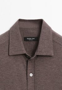Brun tekstureret skjortekrave med knapper og øvre bryst, med synligt mærkelabel "Massimo Dutti" på hvid baggrund.